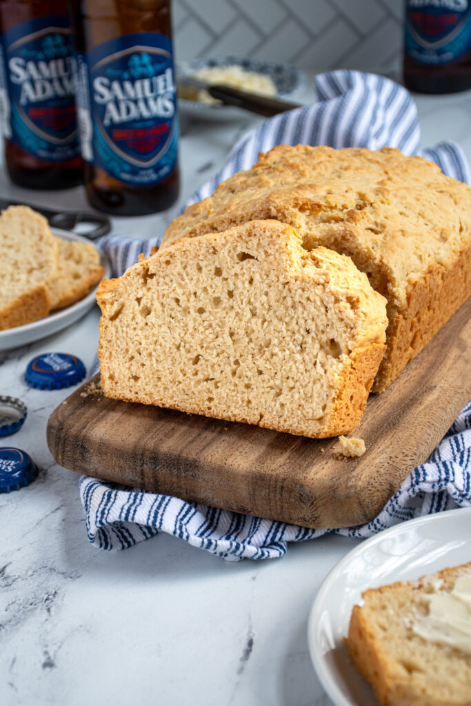 A slice of beer bread on a cutting board propped up against a loaf of easy beer bread.