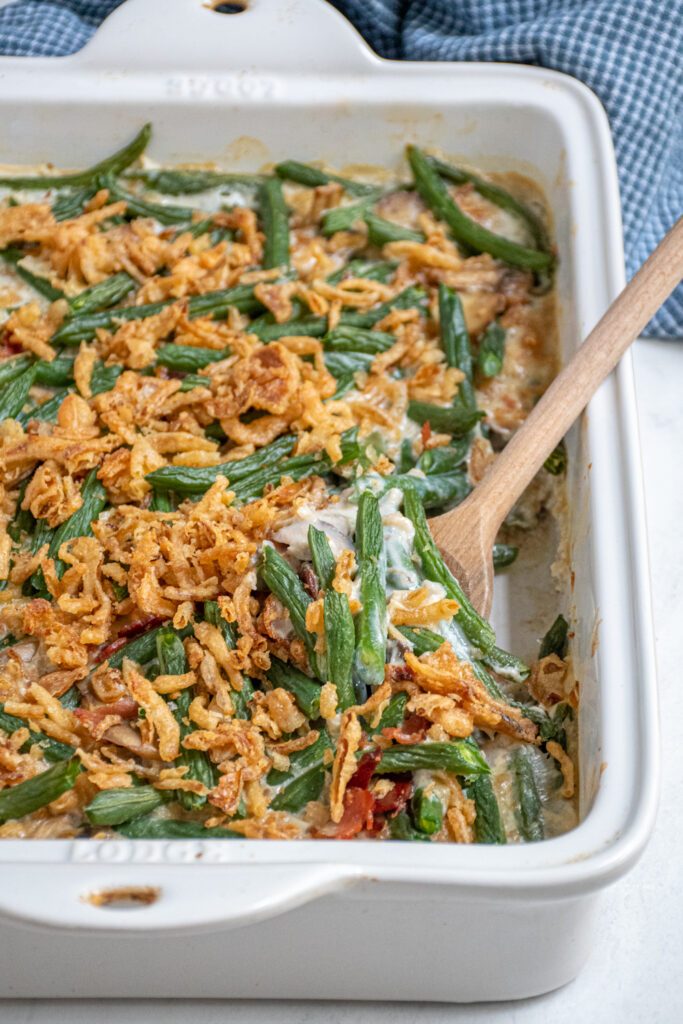 A white casserole dish with fresh green bean casserole with a serving spoon scooping some out of the dish.
