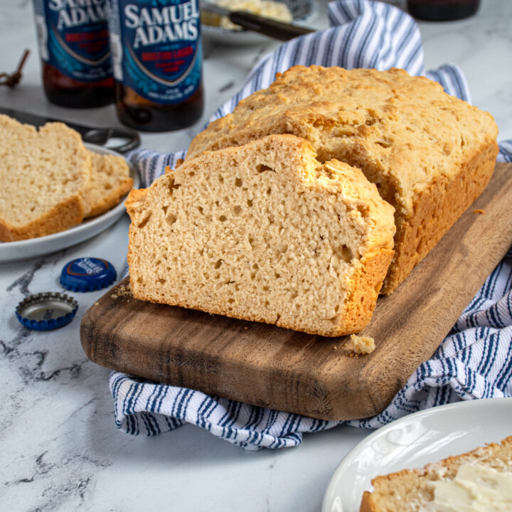 a slice and loaf of beer bread on a cutting board surrounded by slices of bread and a few beer bottles.