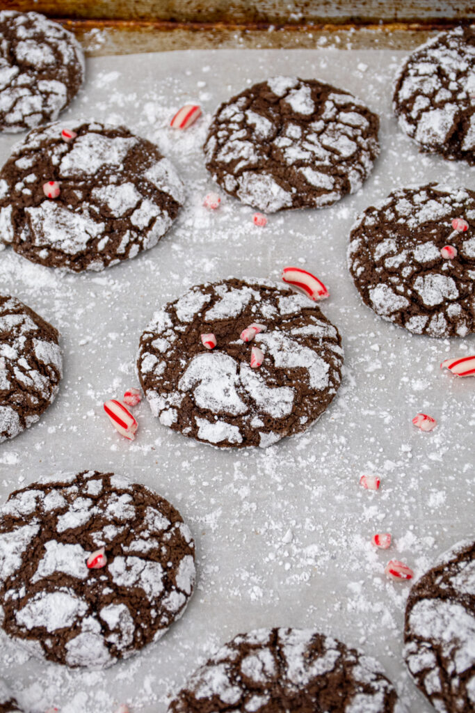 Sheet pan covered in parchment paper with black and white chocolate peppermint crinkle cookies spread out garnished with bits of candy canes.