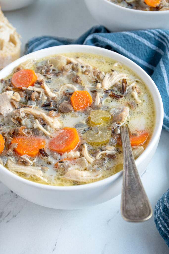 Close up of a white bowl with a spoon filled with slow cooker chicken wild rice soup.