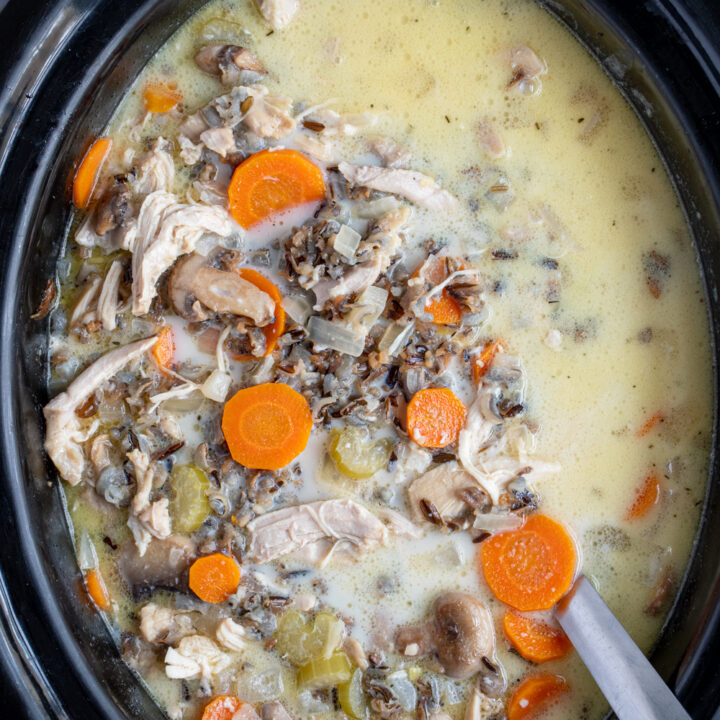 Black crockpot filled with chicken wild rice soup with a ladle showing off wild rice, carrots, celery, and chicken.