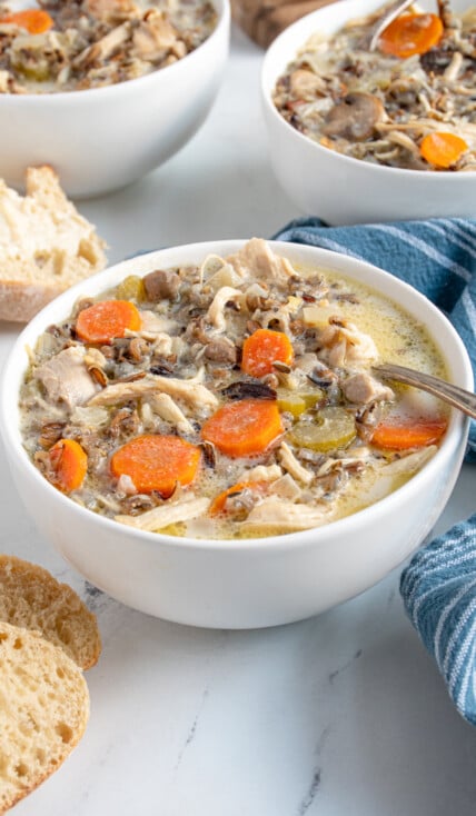 A white bowl with a spoon filled with crockpot chicken wild rice soup showing off carrots, wild rice, and chicken.