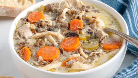 A white bowl with a spoon filled with crockpot chicken wild rice soup showing off carrots, wild rice, and chicken.