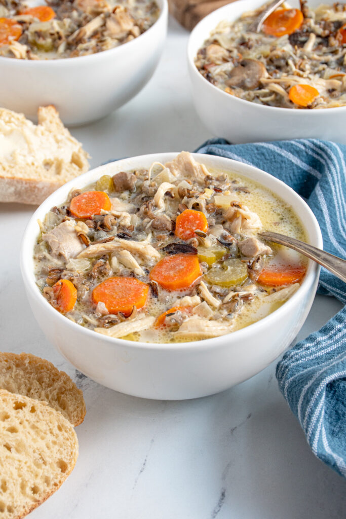A white bowl with a spoon filled with crockpot chicken wild rice soup showing off carrots, wild rice, and chicken.