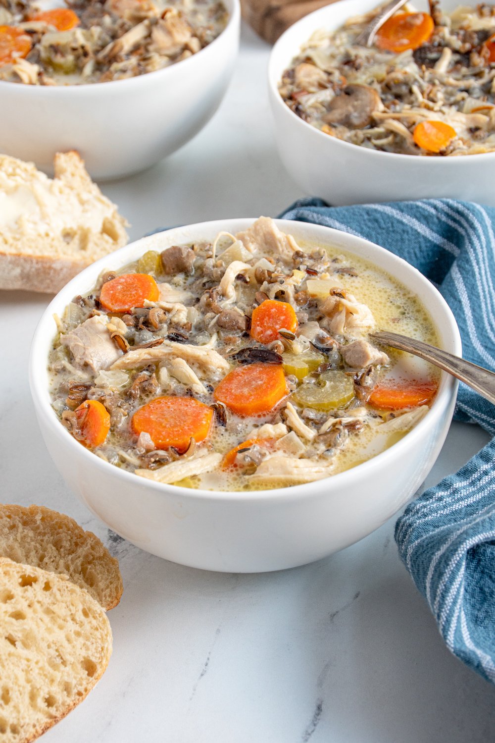 A white bowl with a spoon filled with crockpot chicken wild rice soup showing off carrots, wild rice, and chicken.