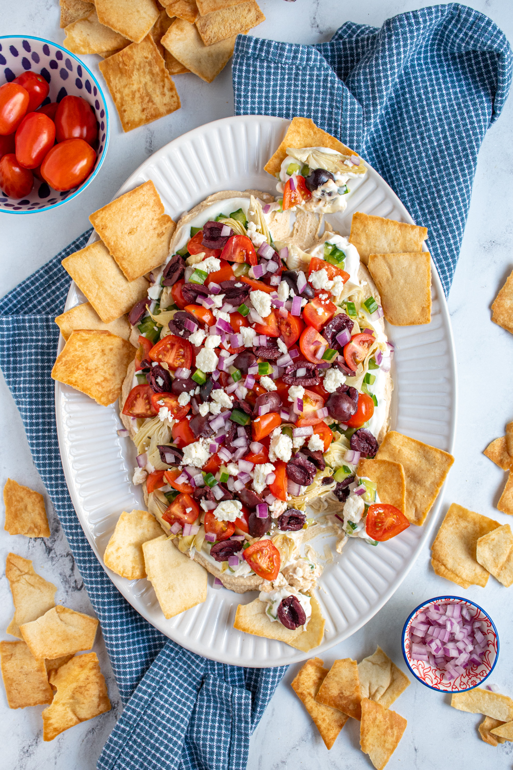 White platter full of greek layer dip with pita chips scooping the dip off of the platter.
