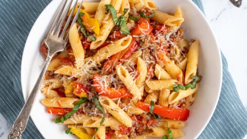 Overhead view of a white bowl with a fork filled with sausage and pepper penne pasta, garnished with parmesan cheese.