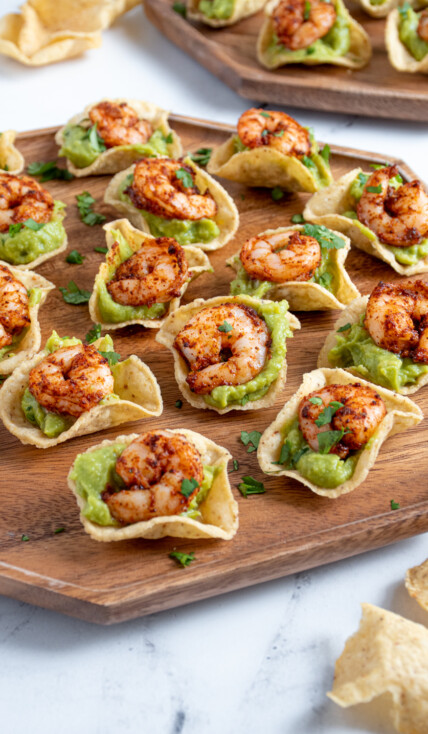 A wooden platter filled with many shrimp guacamole bites garnished with little pieces of cilantro.