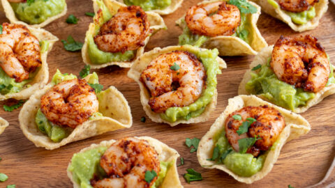 A wooden platter filled with many shrimp guacamole bites garnished with little pieces of cilantro.