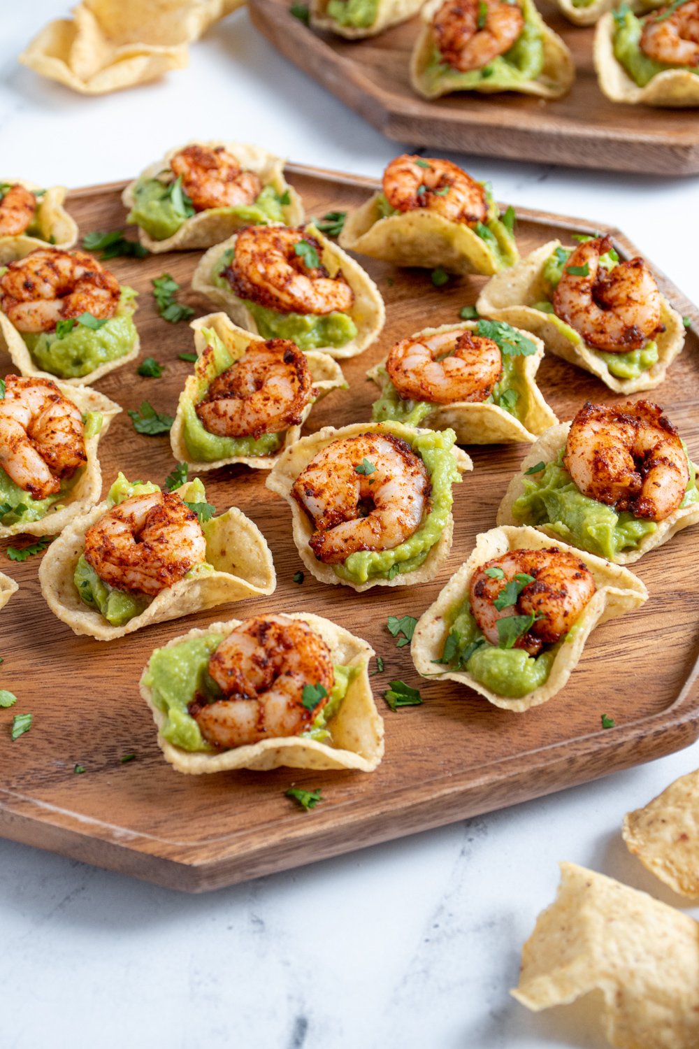 A wooden platter filled with many shrimp guacamole bites garnished with little pieces of cilantro.