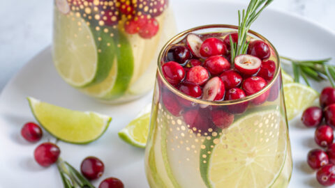 Two stemless wine glasses full of white wine Christmas sangria with pears, limes, and cranberries.