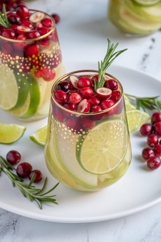 A stemless wine glass filled with White Christmas sangria filled with green pears, limes, and fresh cranberries.