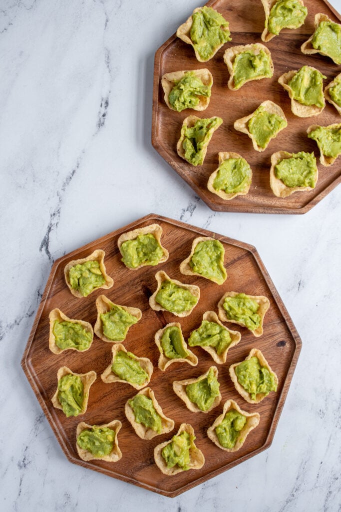Overhead view of two wooden platter holding the chips with guacamole scooped in before getting topped with shrimp.