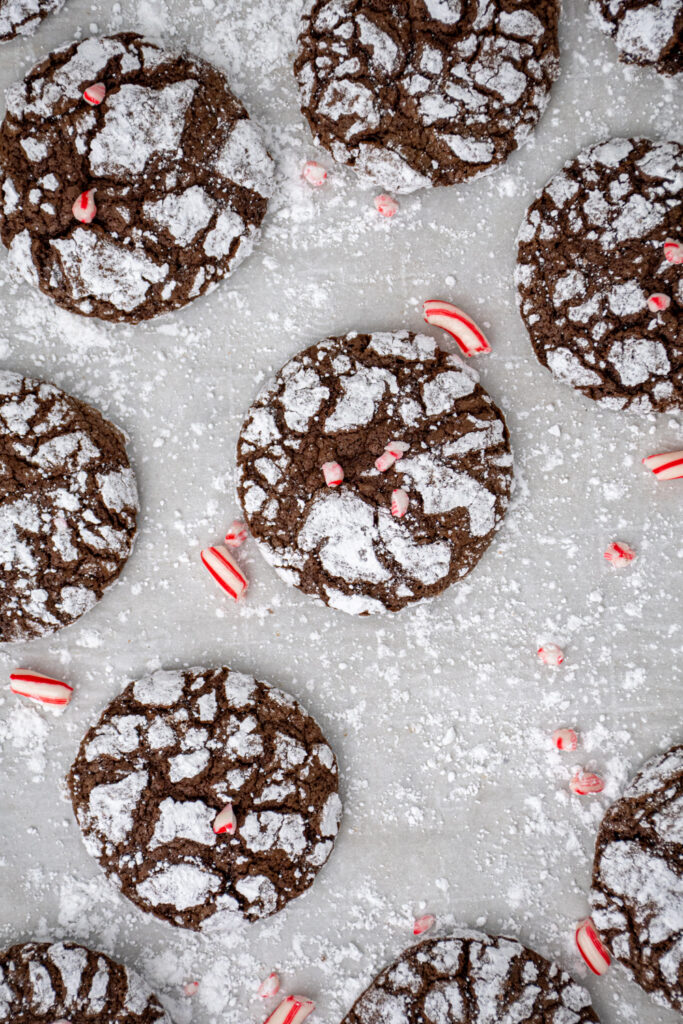 Overhead view of a black and white chocolate peppermint crinkle cookie on a piece of parchment paper garnished with bits of red and white candy canes.