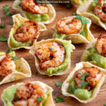 Pinterest Pin with text 'Guacamole Shrimp Bites', image of a wood platter filled with many shrimp guacamole bites.