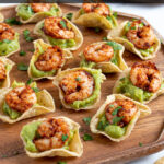 Pinterest Pin with text 'Guacamole Shrimp Bites', image of a wood platter filled with many shrimp guacamole bites.
