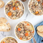 Pinterest Pin with text 'Crockpot Chicken Wild Rice Soup', image of white bowls filled with soup with spoons and bread.