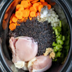 Pinterest Pin with text 'Crockpot Chicken Wild Rice Soup', image of a black crockpot with all the ingredients laid out inside before cooking the soup.
