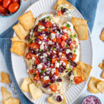 Pinterest Pin with text 'Greek Layer Dip', image of a platter filled with Greek Layered Dip and pita chips.