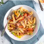 Pinterest Pin with text 'Sausage & Pepper Pasta', image of white bowl filled with penne, bell peppers, and sausage garnished with parmesan cheese.