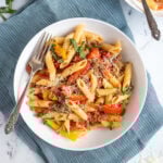 Pinterest Pin with text 'Sausage & Pepper Pasta', image of white bowl filled with penne, bell peppers, and sausage garnished with parmesan cheese.