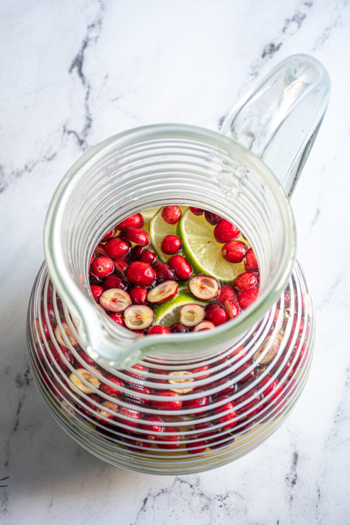 A large pitcher filled with pears, limes, and cranberries topped off with white wine.