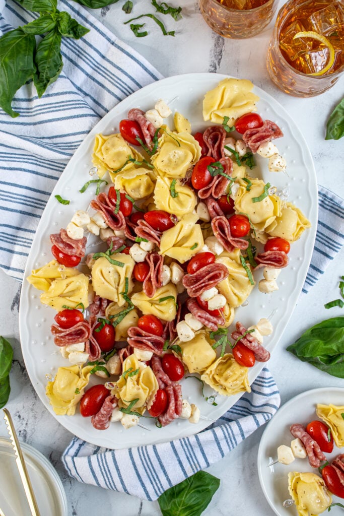 A large white platter filled with colorful tortellini skewers and garnished with basil.