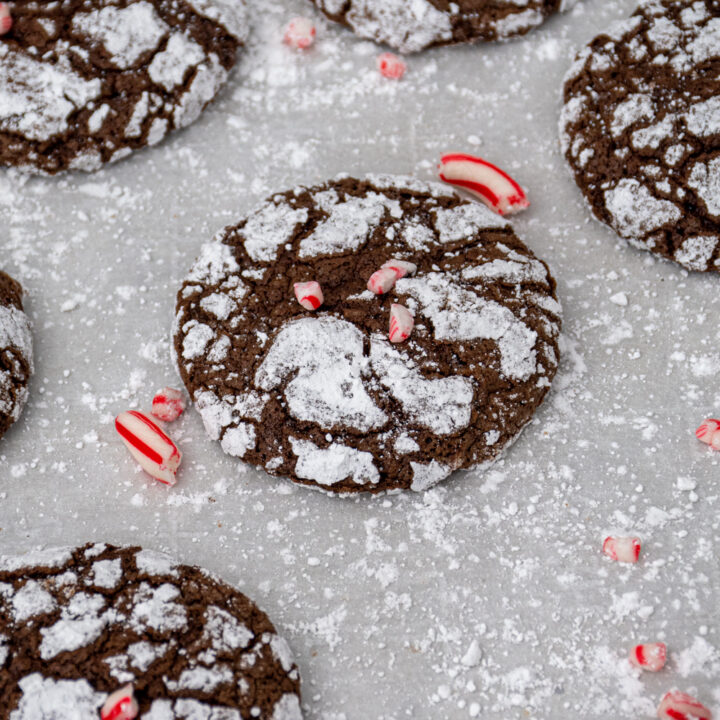 Close up of a chocolate peppermint crinkle cookie sitting on parchment paper garnished with crushed candy canes.