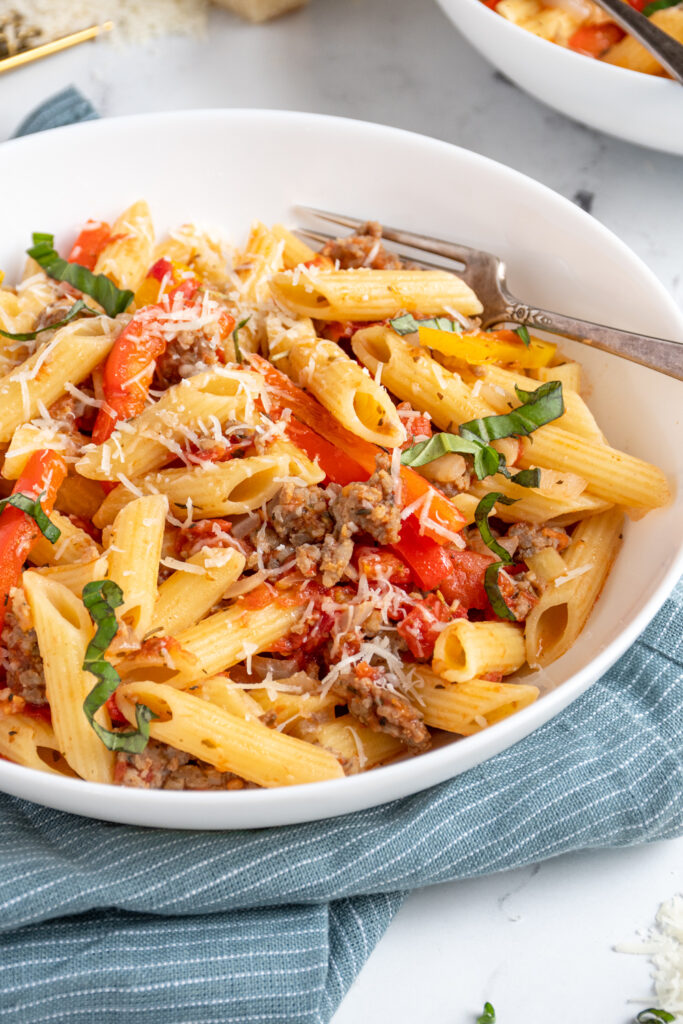 Close up of penne pasta and peppers in a bowl with a fork garnished with parmesan cheese.