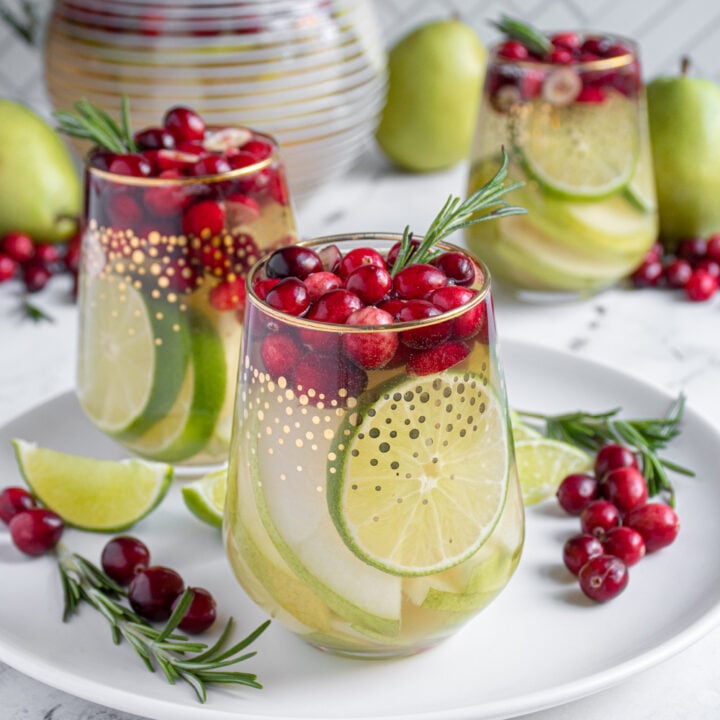 Stemless glasses with white winter sangria filled with pears, limes, cranberries, and topped off with fresh rosemary.