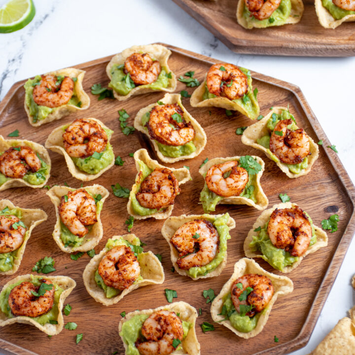 A wood platter filled with shrimp guacamole bites garnished with fresh cilantro.