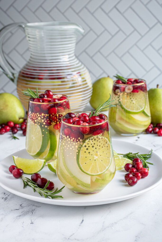 A shot of a stemless wine glass filled with pears, limes, and cranberries filled with White Christmas sangria.