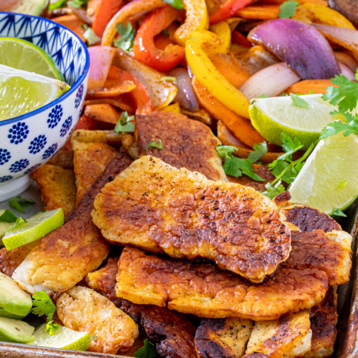 Close up of golden brown cooked halloumi on a tray next to fajita veggies and lime wedges.