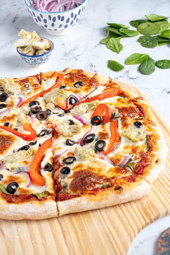 Close up of homemade veggie pizza topped with olives, bell peppers, artichokes, and red onions.