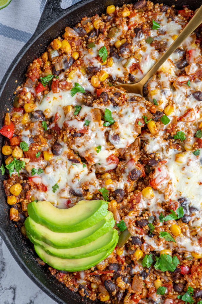 close up of southwest quinoa topped with melted cheese and avocado slices.