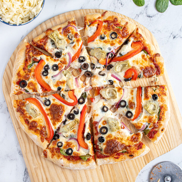 A homemade veggie pizza on a pizza peel cut into pieces with melty mozzarella.