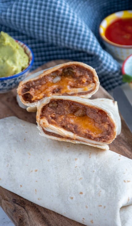 Close up of refried bean burrito cut open showing the insides on a cutting board.