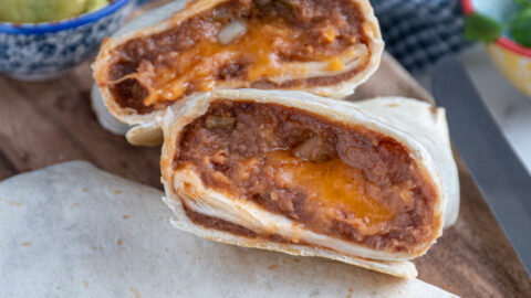 Close up of refried bean burrito cut open showing the insides on a cutting board.