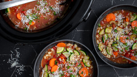 Table top with black bowls and crockpot filled with minestrone soup and garnished with parmesan cheese.