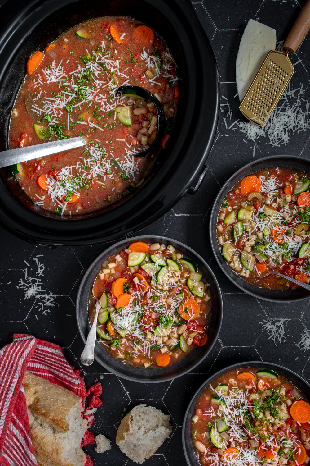 Table top with black bowls and crockpot filled with minestrone soup and garnished with parmesan cheese.
