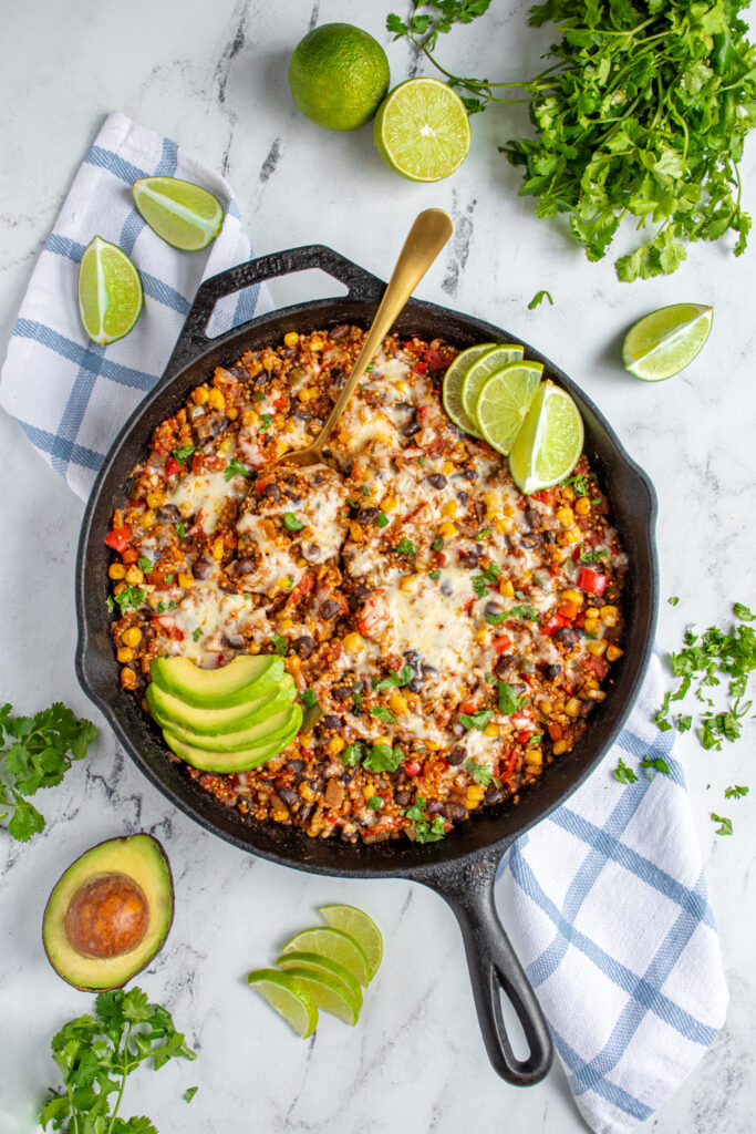 Flatlay of a black cast iron skillet on a table top with colorful corn and peppers topped with cheese and avocado.