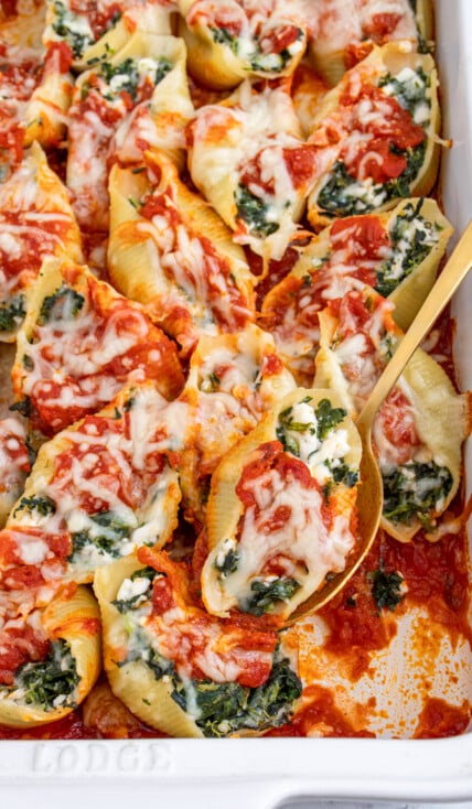 White casserole dish filled with spinach stuffed shells, a spoon taking on out of the dish.