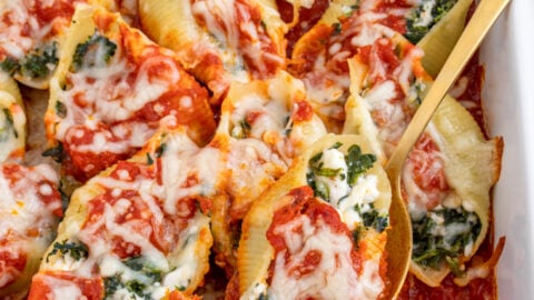 White casserole dish filled with spinach stuffed shells, a spoon taking on out of the dish.