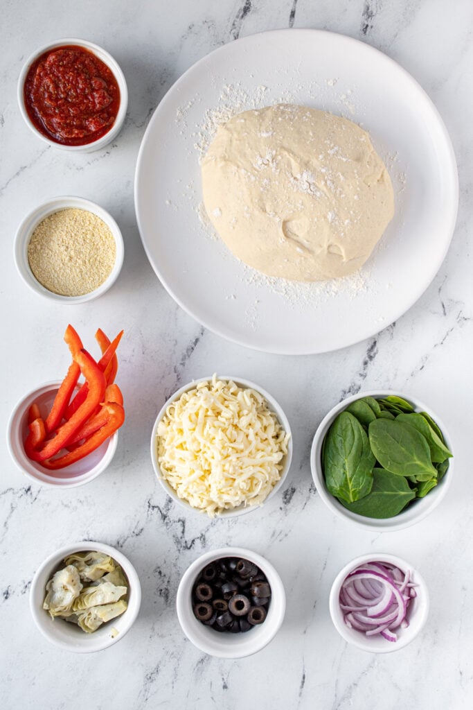 Ingredients needed to make homemade veggie pizza laid out on a tabletop.