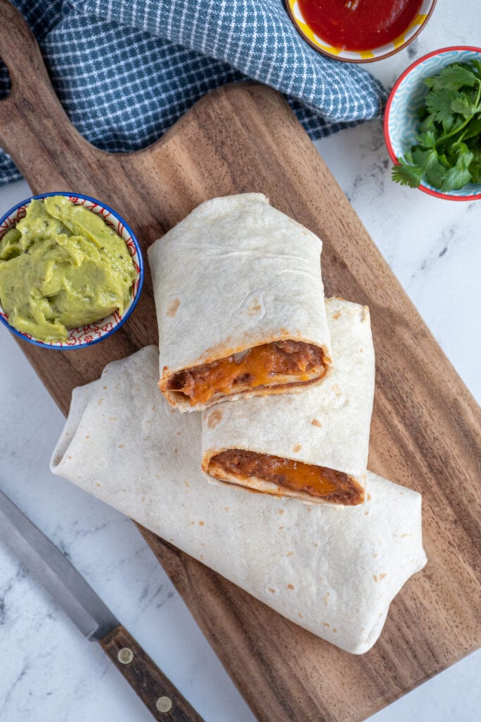 Overhead view of bean burritos, one whole and two halves on a cutting board.