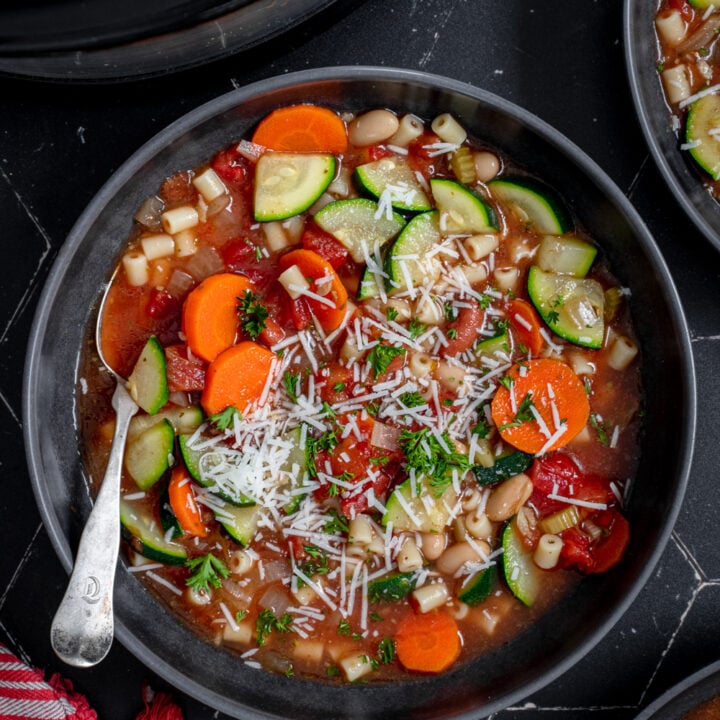 A black bowl with crockpot minestrone soup garnished with parmesan cheese and fresh parsley.