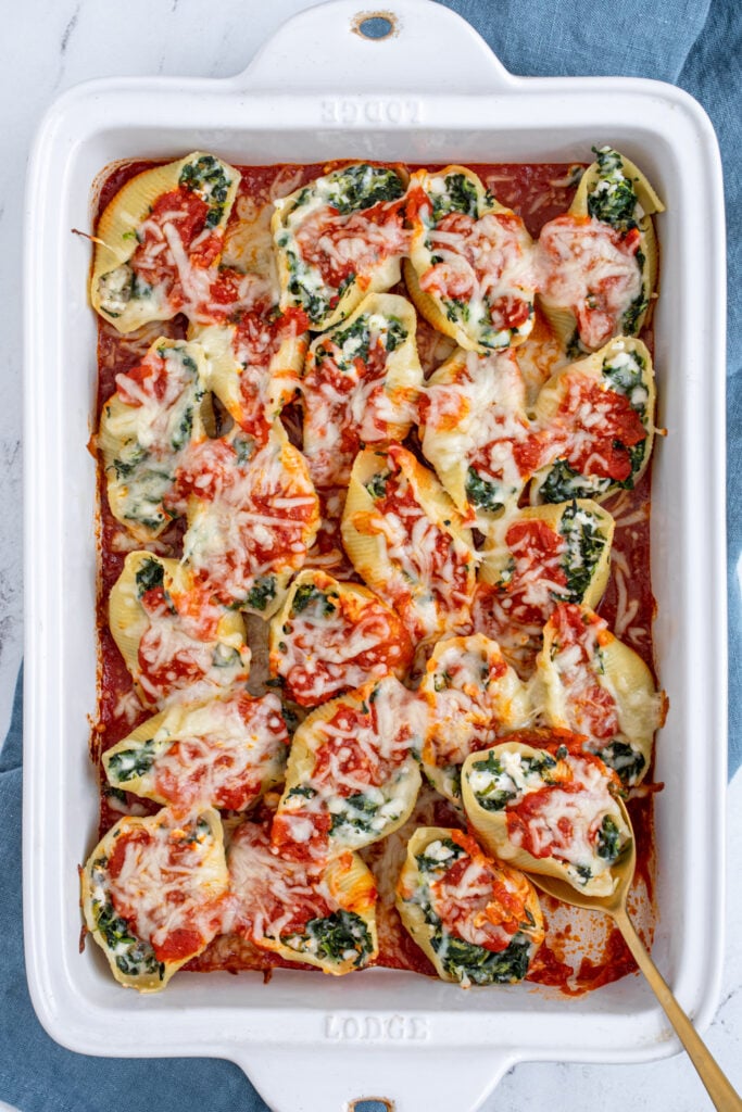 Overhead dish of spinach stuffed shells with a spoon scooping one out.