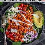 Pinterest Pin with text 'Buffalo Chickpea Salad', image of a brightly colored buffalo chickpea salad in a black bowl.