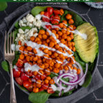 Pinterest Pin with text 'Buffalo Chickpea Salad', image of a brightly colored buffalo chickpea salad in a black bowl.